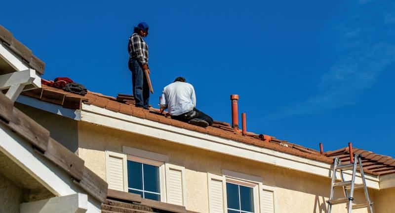 Low angle shot of builders fixing a tiled roof against blue sky