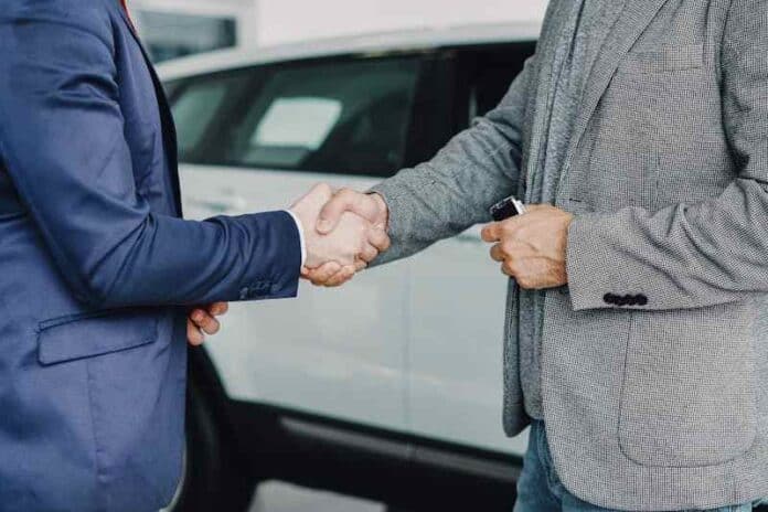 Two businessmen shaking hands in a car dealership